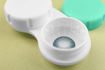 Case with blue contact lenses on light green background, closeup