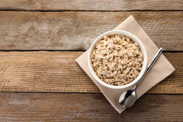 Tasty boiled oatmeal in bowl and spoon on wooden table, top view. Space for text