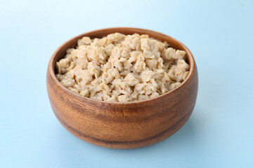 Tasty boiled oatmeal in bowl on light blue background, closeup