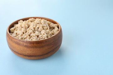 Tasty boiled oatmeal in bowl on light blue background, space for text