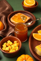Jar and toast with sweet pumpkin jam on green wooden background