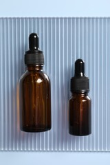 Bottles of cosmetic serum on light blue background, top view