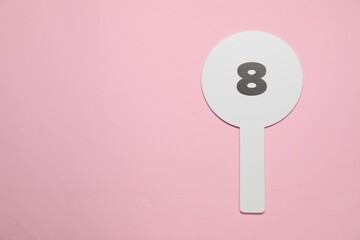 Auction paddle with number 8 on pink background, top view. Space for text