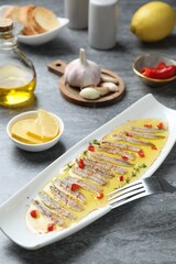 Tasty pickled anchovies with spices and products on gray table