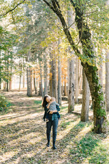 Fototapeta na wymiar Smiling mother with a little girl in her arms walks through the forest
