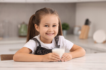 Cute girl with glass of milk at white table in kitchen