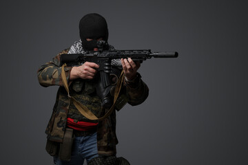 Portrait of a militant from the Middle East, wearing a black balaclava and camo field attire, holding a rifle, set against a gray backdrop