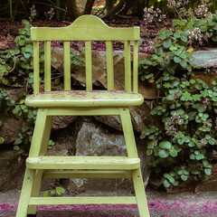 Silla infantil para niño de color verde, con flores violetas sobre la silla y de fondo con piedras y en regadera de color verde