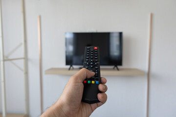 Close up Television remote control in hand man pointing to tv set and turning it on or off. select...