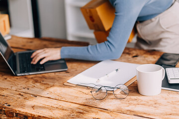 Startup SME small business entrepreneur of freelance Asian woman wearing apron using laptop and box to receive and review orders online to prepare to pack sell to customers, online sme business ideas.