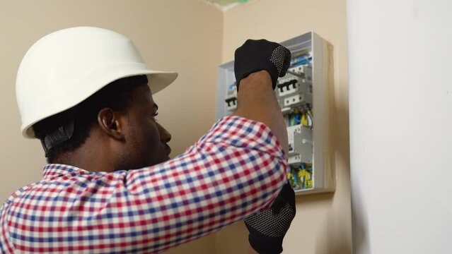 Professional african american electrician in a hard hat and plaid shirt installing an electrical box in a wall
