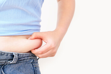 Female hand holding excessive belly fat on white background, overweight concept.