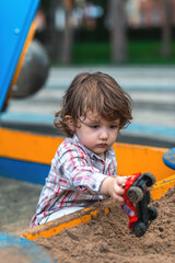 little boy playing in the sandbox with a car