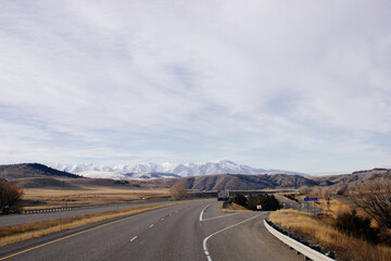 Beautiful landscape with a road among yellow dry grass and snow-covered mountains on the horizon.