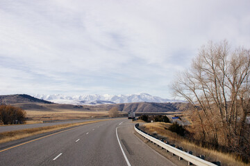 Beautiful landscape with a road among yellow dry grass and snow-covered mountains on the horizon.