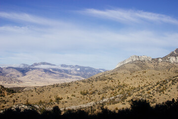 Steep highway in the mountains among huge rocks and high mountains on the horizon on a sunny day. Beautiful blue sky with clouds over mountains and asphalt road. USA highways