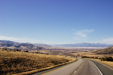 Steep highway in the mountains among huge rocks and high mountains on the horizon on a sunny day. Beautiful blue sky with clouds over mountains and asphalt road. USA highways