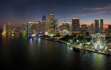 Aerial view of Skyviews Miami Observation Wheel at Bayside Marketplace with reflections in Biscayne Bay water and high illuminated skyscrapers of Brickell, city's financial center at night