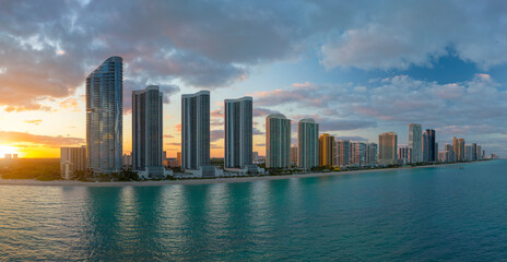 Aerial view of Sunny Isles Beach city with luxurious highrise hotels and condos on Atlantic ocean shore at sunset. American tourism infrastructure in southern Florida