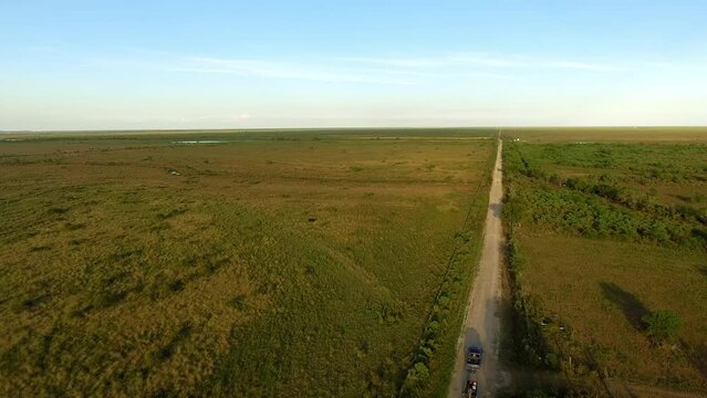 Aerial Forward Shot Of Pickup Truck And Old Boat Moving On Road Amidst Green Meadow Landscape During Sunny Day - Bayou, Louisiana