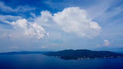 White clouds over a tropical island. Large cumulus clouds over a tropical island and blue sea.