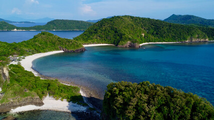 Fototapeta na wymiar Tropical island with a sandy beach and jungle. Aerial view of a tropical island's hilly coastline, lagoon, beach and tropical rainforest.