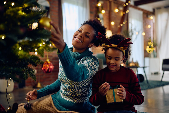 Happy Black Woman Decorating Christmas Tree With Her Daughter At Home.