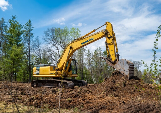 NISSWA, MN – 10 MAY 2023: A yellow Komatsu excavator at a future new home building site with its bucket resting on a pile of dirt.