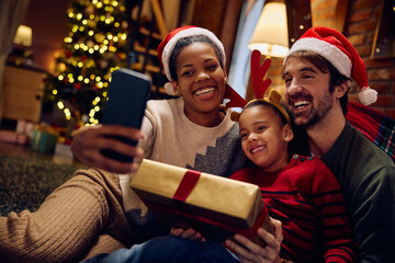 Happy parents with small daughter taking selfie with cell phone at Christmas.