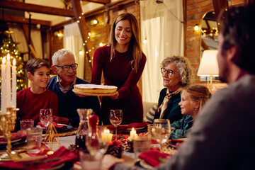 Happy woman brining pie at dinning table while having Christmas dinner with her family.