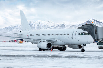 Fototapeta na wymiar White passenger airliner at the jetway at winter airport apron on the background of high scenic mountains