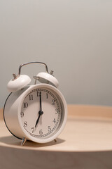 Close-up of a round white alarm clock on a table in the bedroom. The hands on the clock show seven...