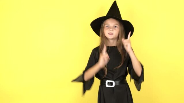 A little girl in a Halloween witch costume dances and shows emotions on a yellow studio background