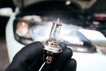 Car halogen bulb in auto mechanic hand with a car blurred background , H4 type , Car parts concept