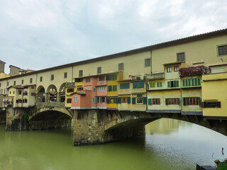 Fototapeta na wymiar Scenic view of historic medieval Ponte Vecchio bridge with shops spanning the Arno River, Florence, Tuscany, Italy, Europe. Landmark in Italian city on cloudy overcast day. Tourist travel destination
