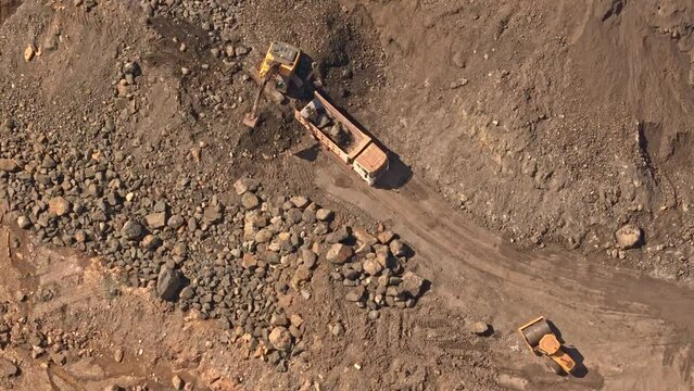 A yellow digger moving dirt and earth into the back of a truck located at a gold and silver mine in Mainit, Philippines. Aerial drone shot, daytime. 