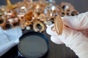 Pawnshop worker verify jewellery on many golden and silver jewelleries and money background. Customers Buy and Sell Precious Metals, Jewels, Ancient Coins and Second Hand Appliances. - obrazy, fototapety, plakaty