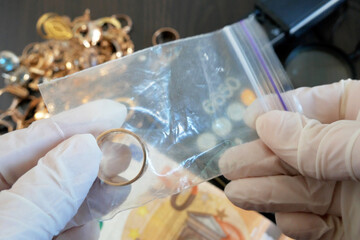 Pawnshop worker packing a gold wedding ring on many golden and silver jewelleries and jewelry scales background, top view - obrazy, fototapety, plakaty