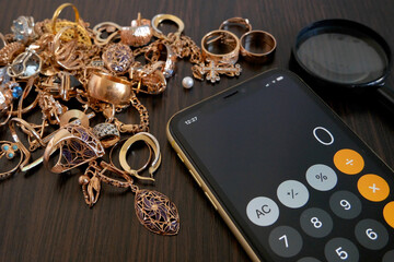 Pawnshop concept, calculator, a lot of gold jewelry and a magnifying glass on a dark wooden table, top view,