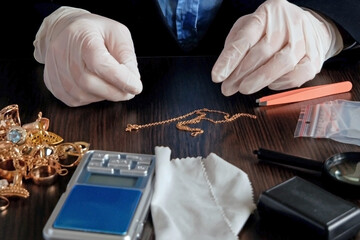 Pawnshop worker verify golden jewelry on many golden and silver jewelleries, scales and money background. Customers Buy and Sell Precious Metals, Jewels, Ancient Coins and Second Hand Appliances.