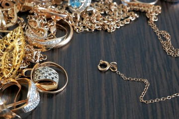 a lot of gold jewelry chains, rings, earrings, bracelets, lie on a dark wooden table, pawnshop...
