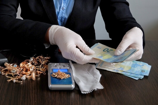 pawnshop worker counts money for gold jewelry on many golden and silver jewelleries background. Customers Buy and Sell Precious Metals, Jewels, Ancient Coins and Second Hand Appliances. Closeup