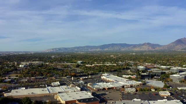 Left trucking aerial drone extreme wide landscape shot of the Salt Lake county valley covered in buildings, busy roads, and colorful autumn trees on a warm sunny fall evening in Utah