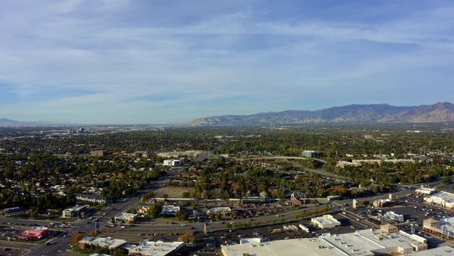 Left trucking aerial drone extreme wide landscape shot of the Salt Lake county valley covered in buildings, busy roads, and colorful autumn trees on a warm sunny fall evening in Utah