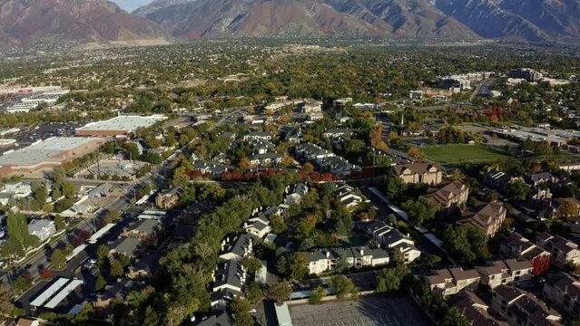 Tilt up dolly in aerial drone wide landscape shot revealing the stunning snowcapped rocky mountains of Utah with Salt Lake county below full of buildings and colorful trees on a warm sunny fall day