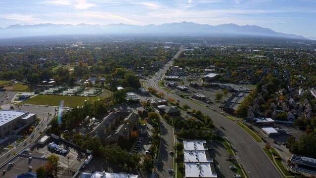 Dolly in tilt up aerial drone extreme wide landscape shot of the Salt Lake county valley covered in buildings, busy roads, and colorful autumn trees surrounded by mountains on a fall evening in Utah