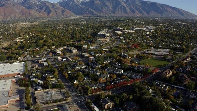 Tilt up descending aerial drone wide landscape shot revealing the stunning snowcapped rocky mountains of Utah with Salt Lake county below full of buildings and colorful trees on a warm sunny fall day