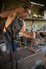 Overview of a blacksmith striking a piece of steel on a anvil.