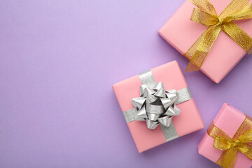 Pink gift boxes with silver and gold bow on purlpe background.