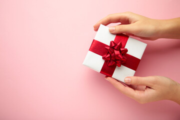 White gift with red bow in female hands on pink background. Space for text.